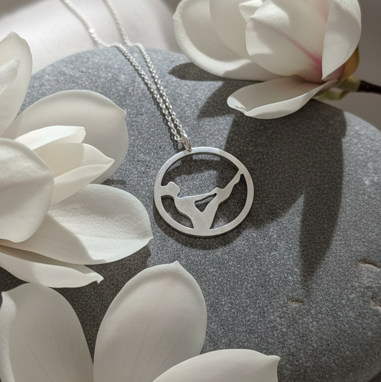 Pilates Teaser sterling silver necklace displayed on a stone with flowers around.